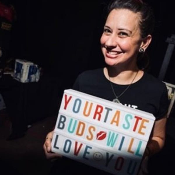 Smiling woman holding a light-up sign that reads "YOUR TASTE BUDS WILL LOVE YOU".