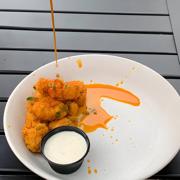 Crispy orange chicken bites with ranch dressing, drizzled with orange sauce on a white plate.
