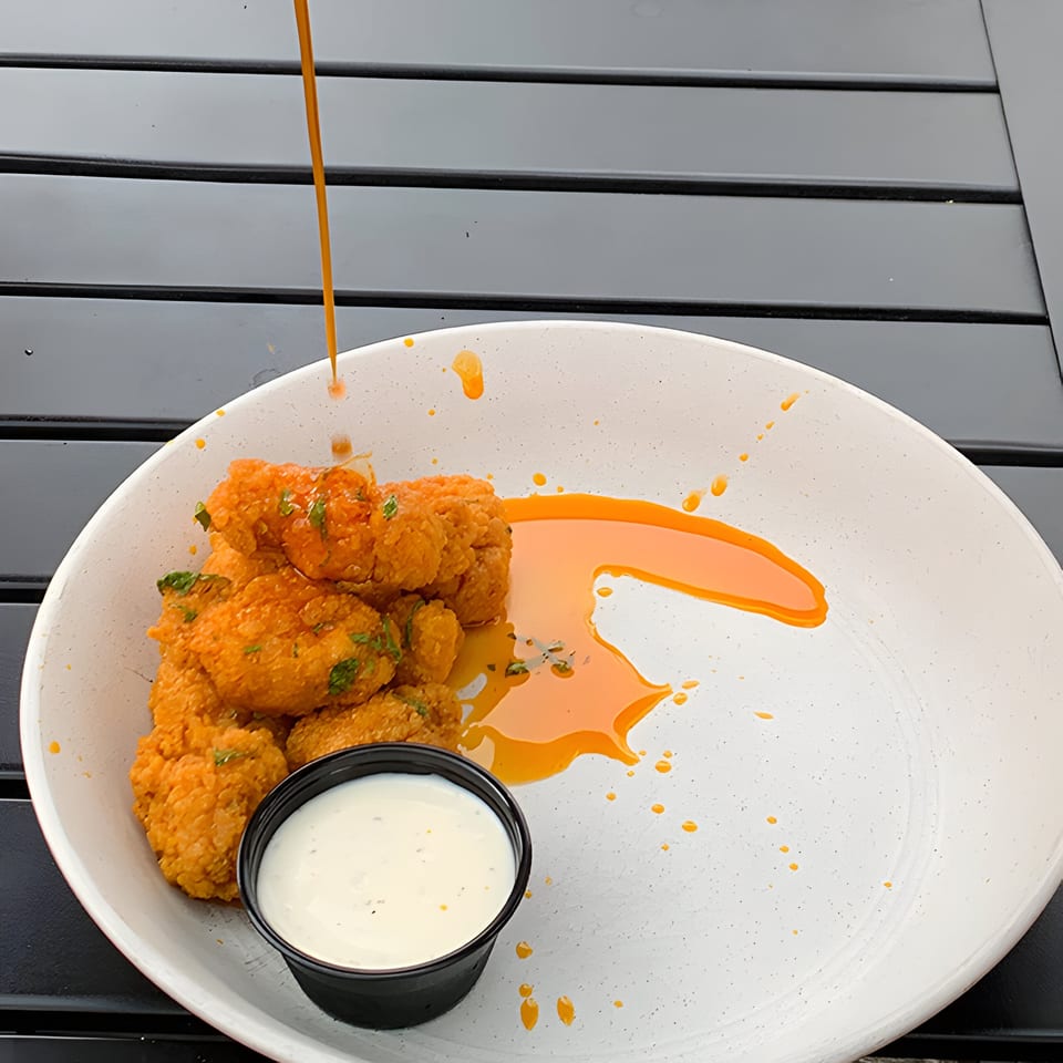 Crispy orange chicken bites with ranch dressing, drizzled with orange sauce on a white plate.