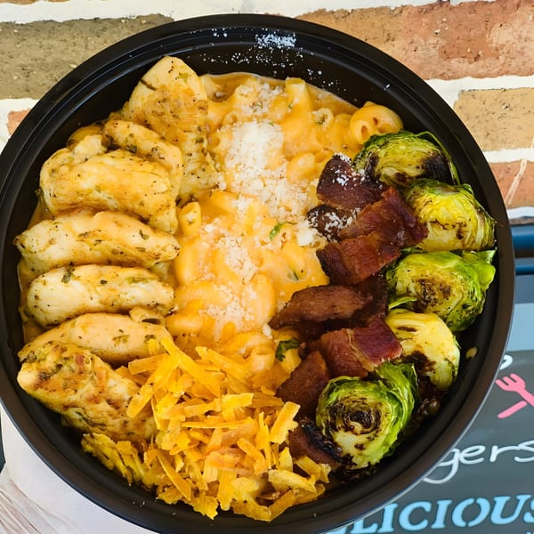 A black bowl filled with mac and cheese, chicken, bacon, roasted brussels sprouts, and shredded cheese.